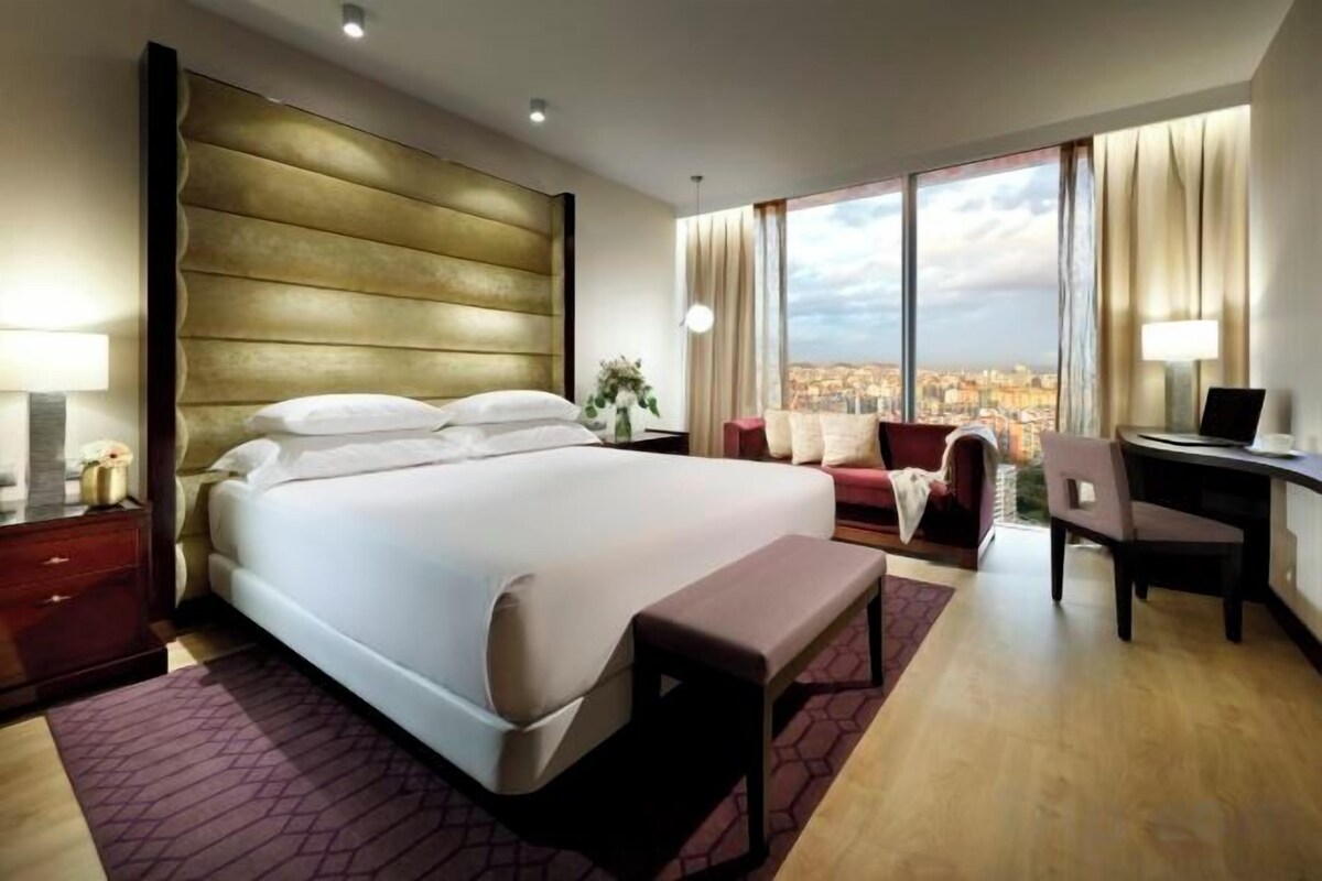 Ein Hotelzimmer mit einem großen Bett, einem Schreibtisch, einem Stuhl und Blick auf die Stadt.