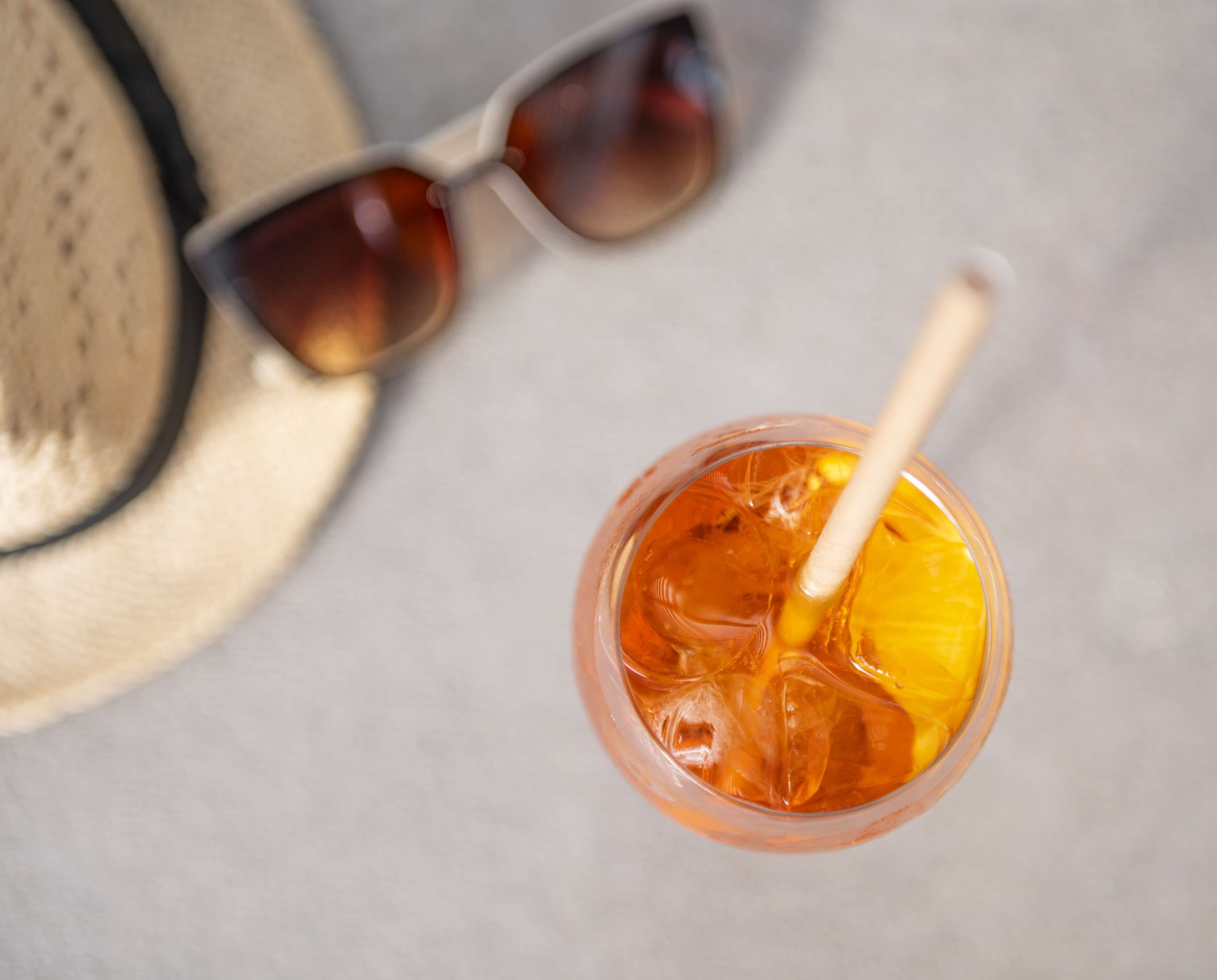 A drink with a straw and a slice of lemon, a pair of sunglasses, and a straw hat.