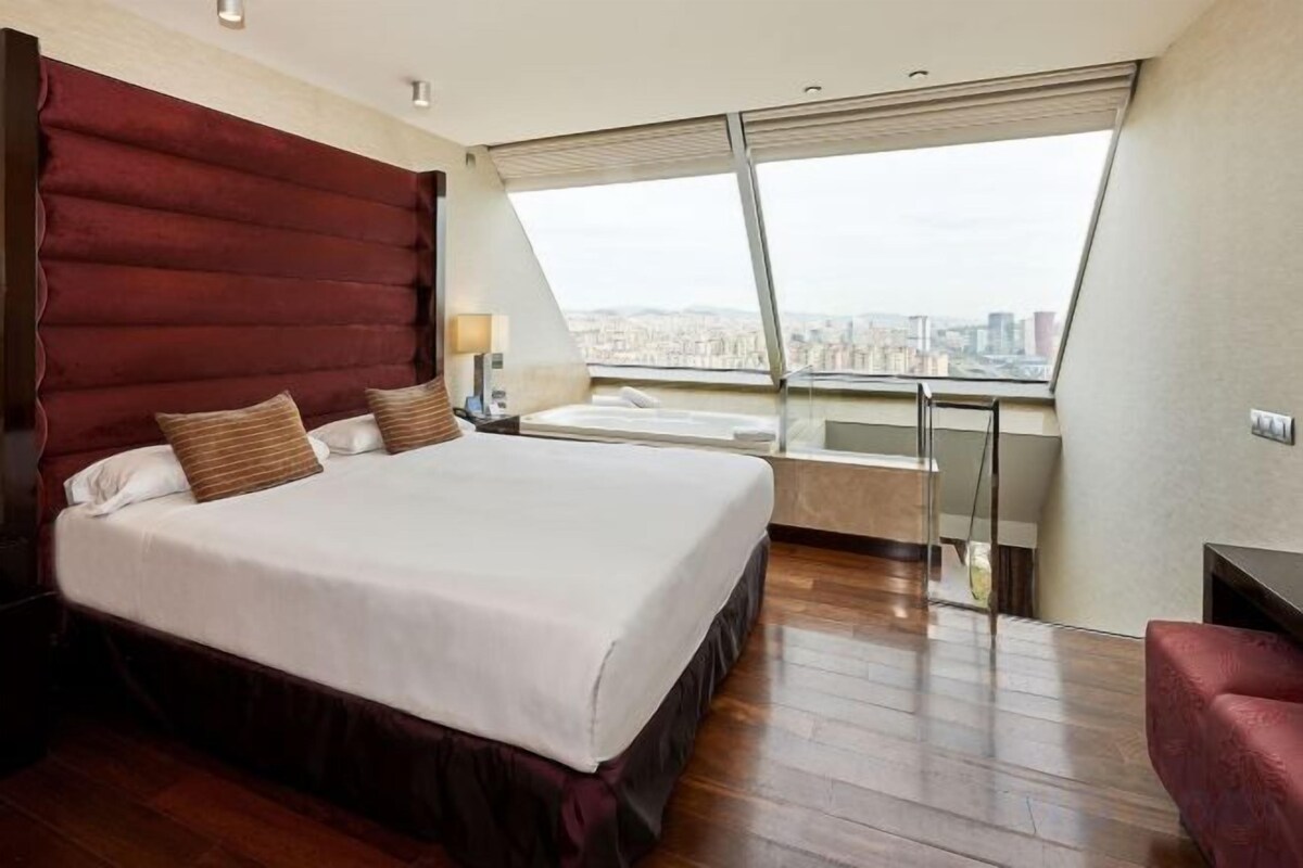 Ein Hotelzimmer mit einem großen Bett, Blick auf die Stadt, einem Balkon und einem roten Sessel.