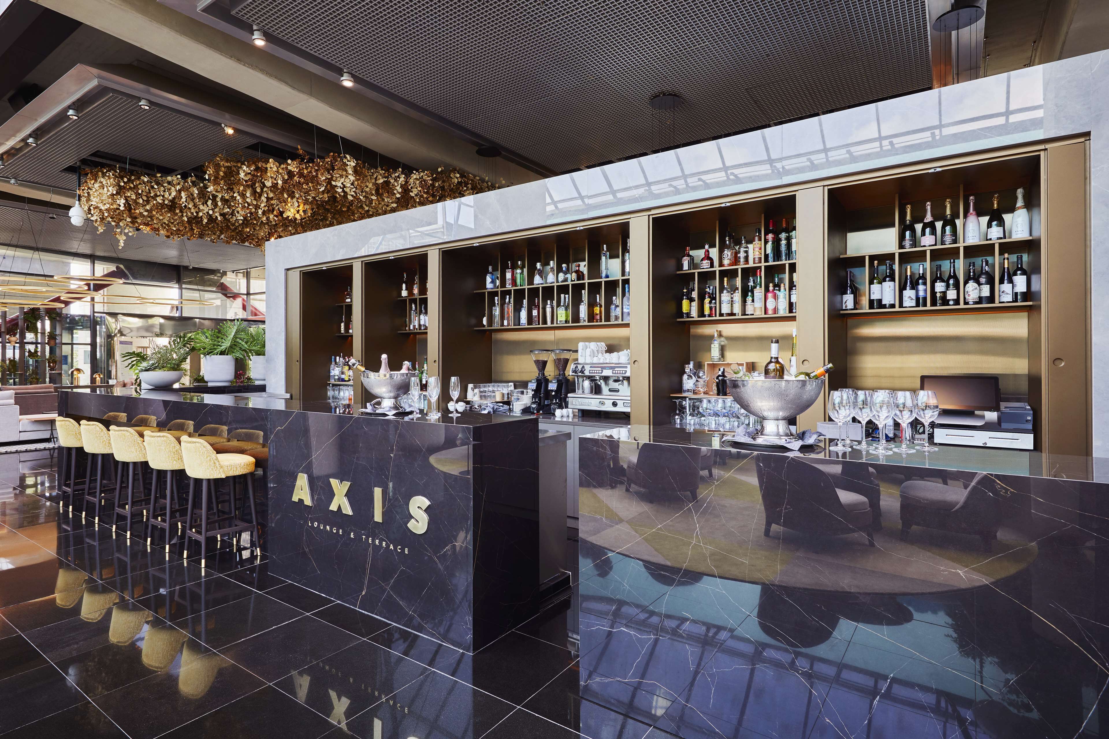 A modern bar area with a marble counter, bar stools, and shelves stocked with bottles.
