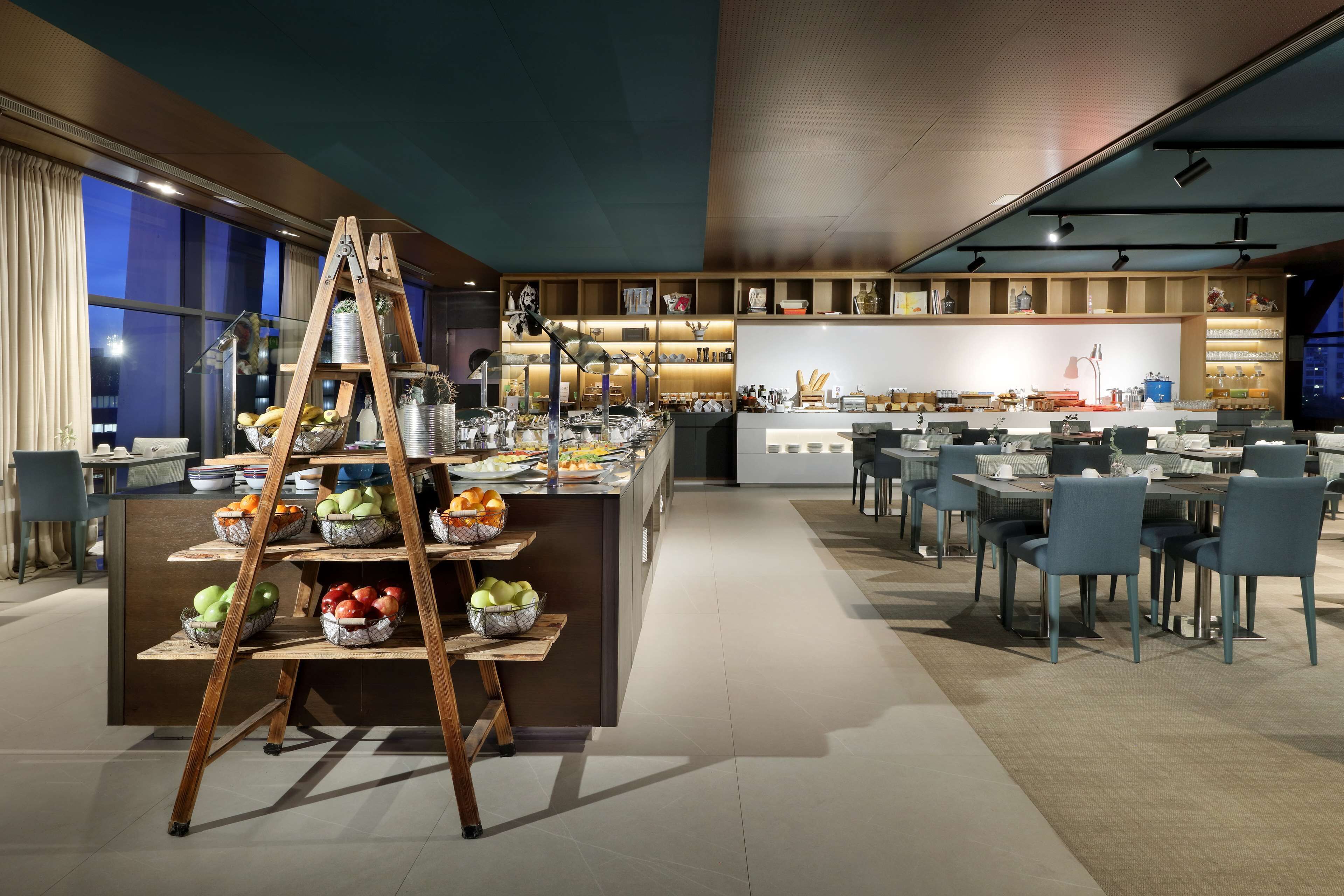 A modern dining area with a central island, multiple seating arrangements, and a variety of food and drink items displayed.