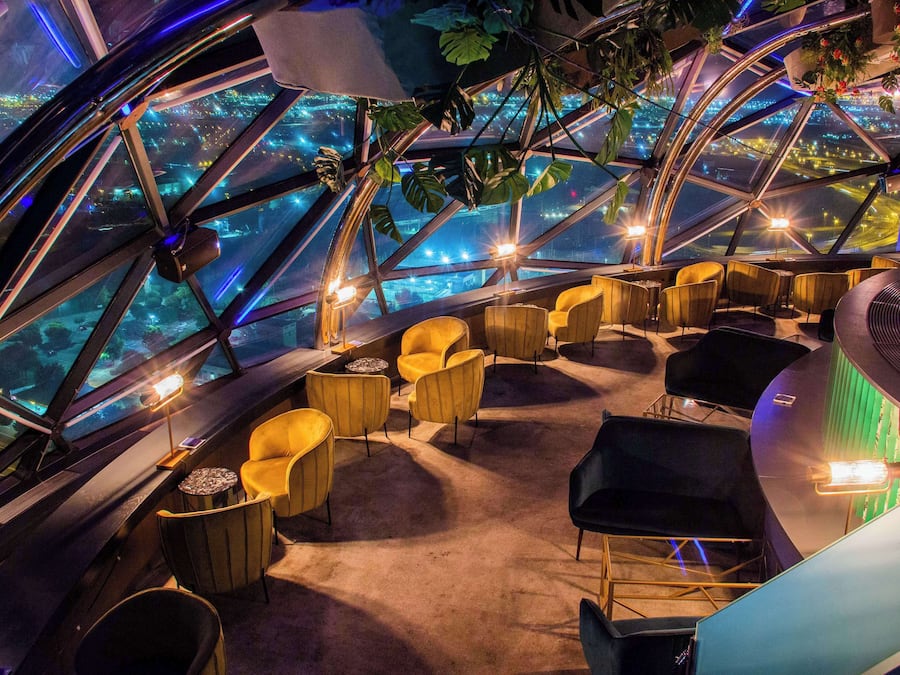 Interior de una cúpula geodésica con asientos y vistas de un paisaje urbano a través de amplias ventanas.
