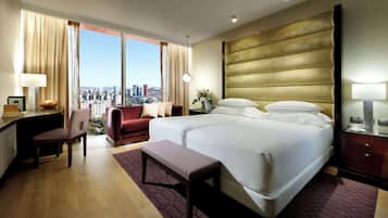 A hotel room with a large bed, a desk, a chair, and a view of the city.
