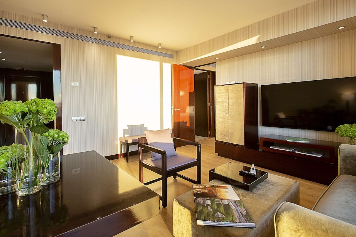 A modern living room with a large flat-screen TV, comfortable seating, and a glass coffee table.