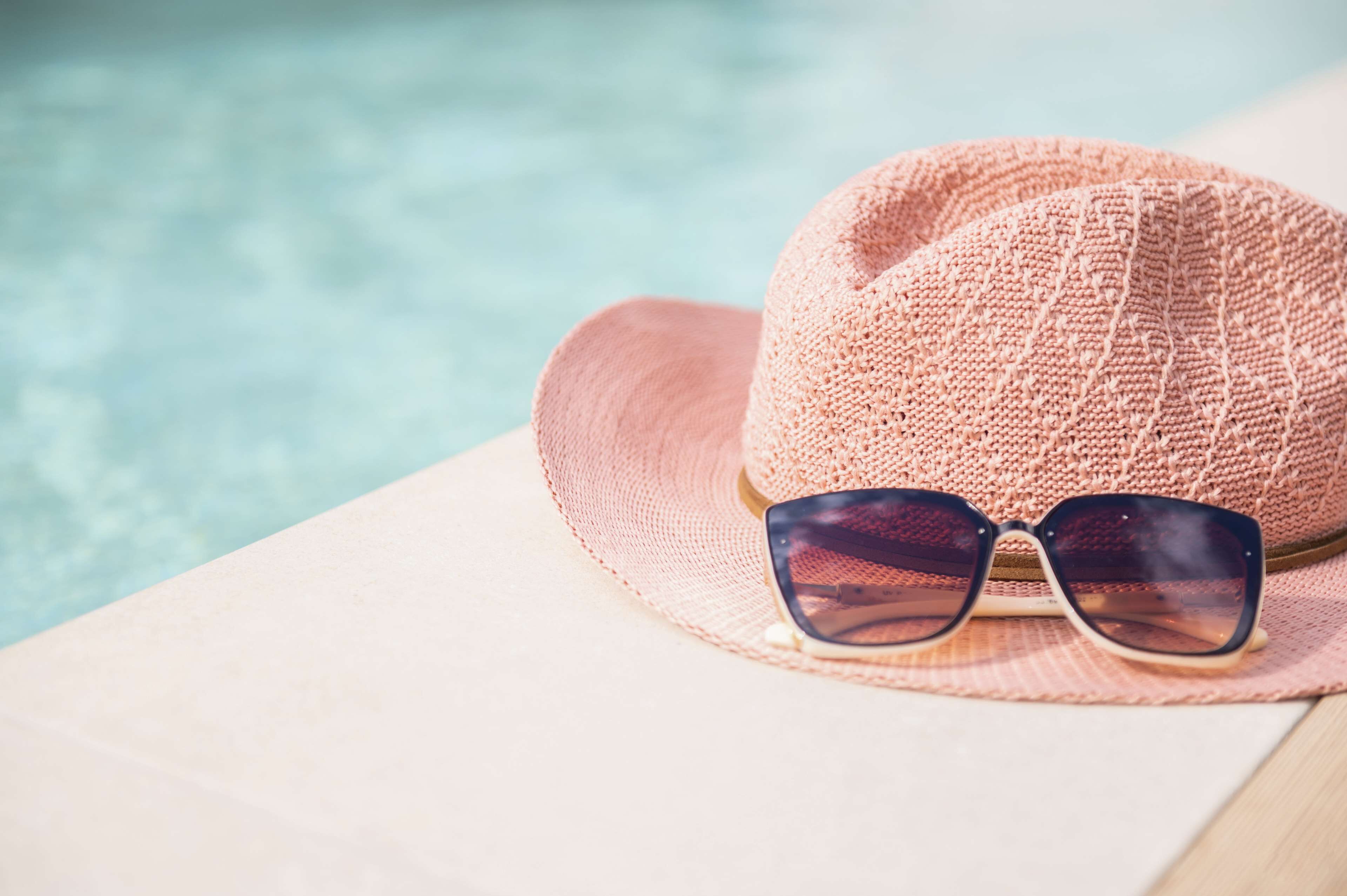 A straw hat and sunglasses on a light-colored surface near a pool.