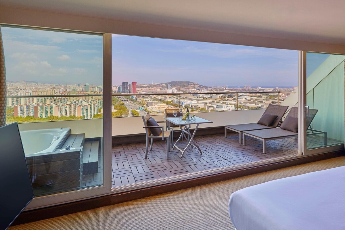 Ein Hotelzimmer mit Balkon, einem Bett, einer Couch, einem Tisch und einer Whirlwanne.
