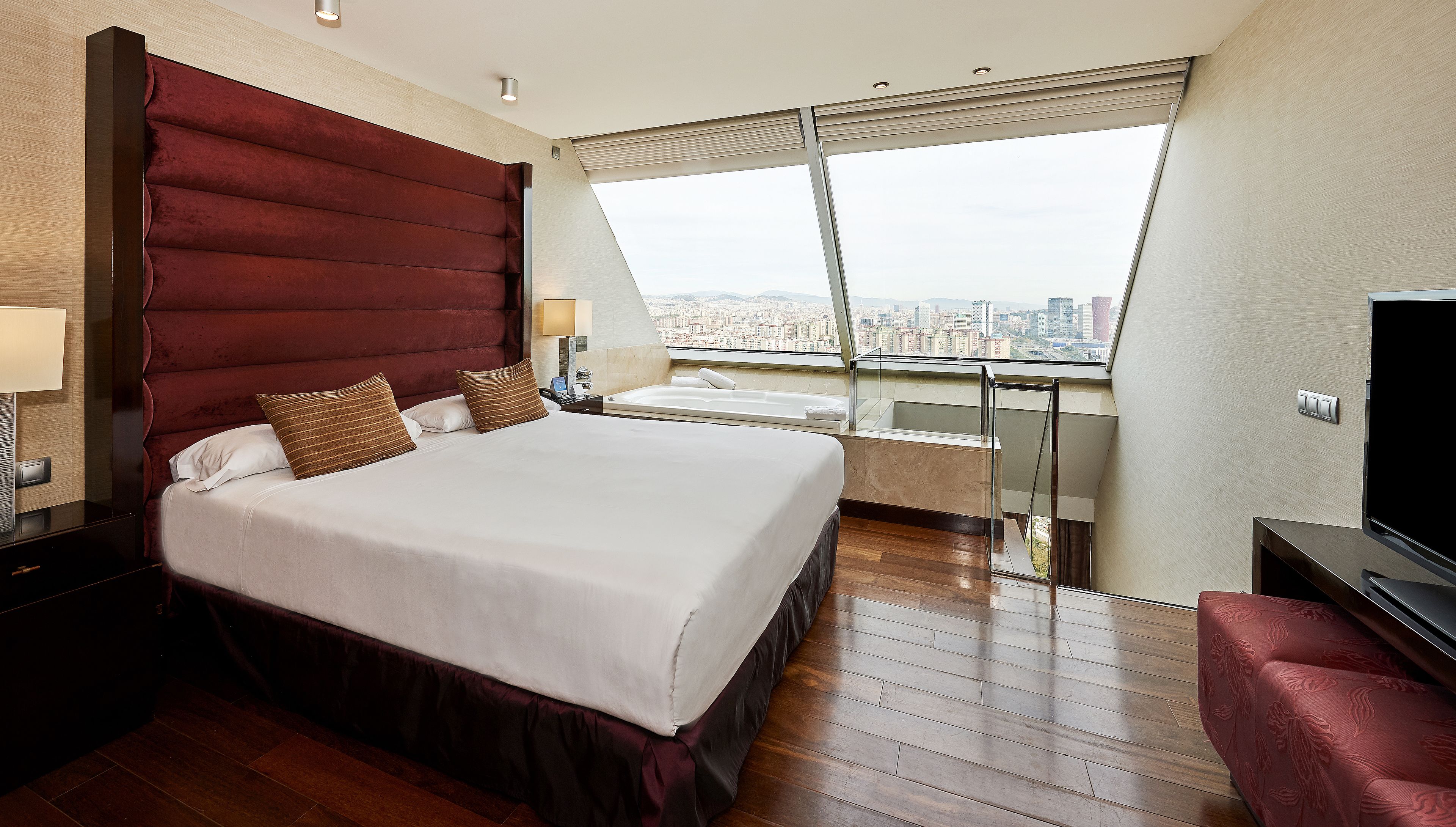 A hotel room with a large bed, a city view, a balcony, and a TV.