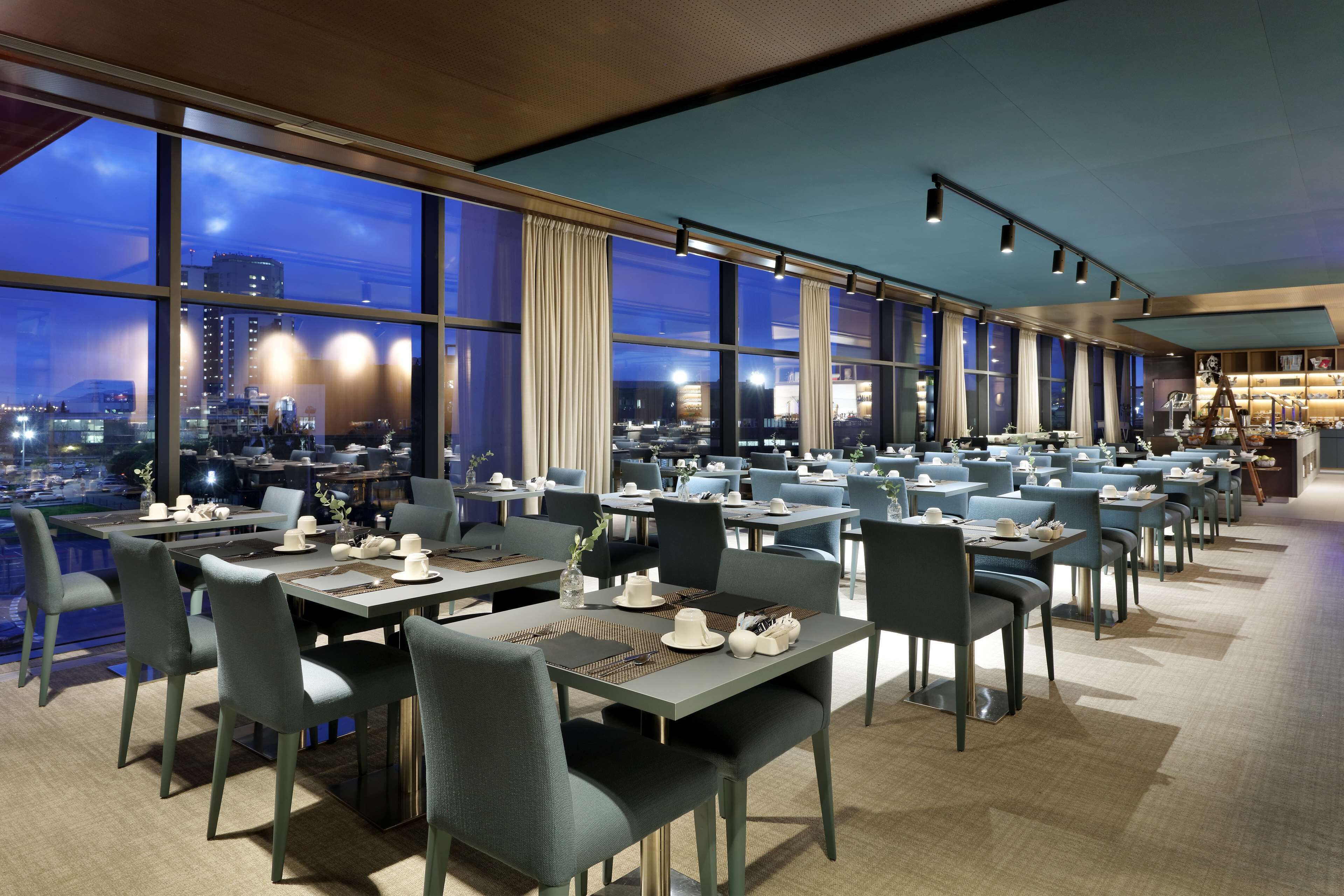 Un restaurant moderne offrant une vue sur la ville, avec des tables et des chaises disposées avec soin, et une ambiance calme et accueillante.