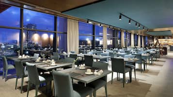 Un restaurant moderne offrant une vue sur la ville, avec des tables et des chaises disposées avec soin, et une ambiance calme et accueillante.