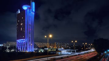 Ein Hochhaus mit beleuchteten blauen Strukturelementen und einem markanten zylindrischen Aufsatz oben.