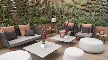 Un área de estar al aire libre con sofás acolchados, mesas redondas y plantas en macetas.