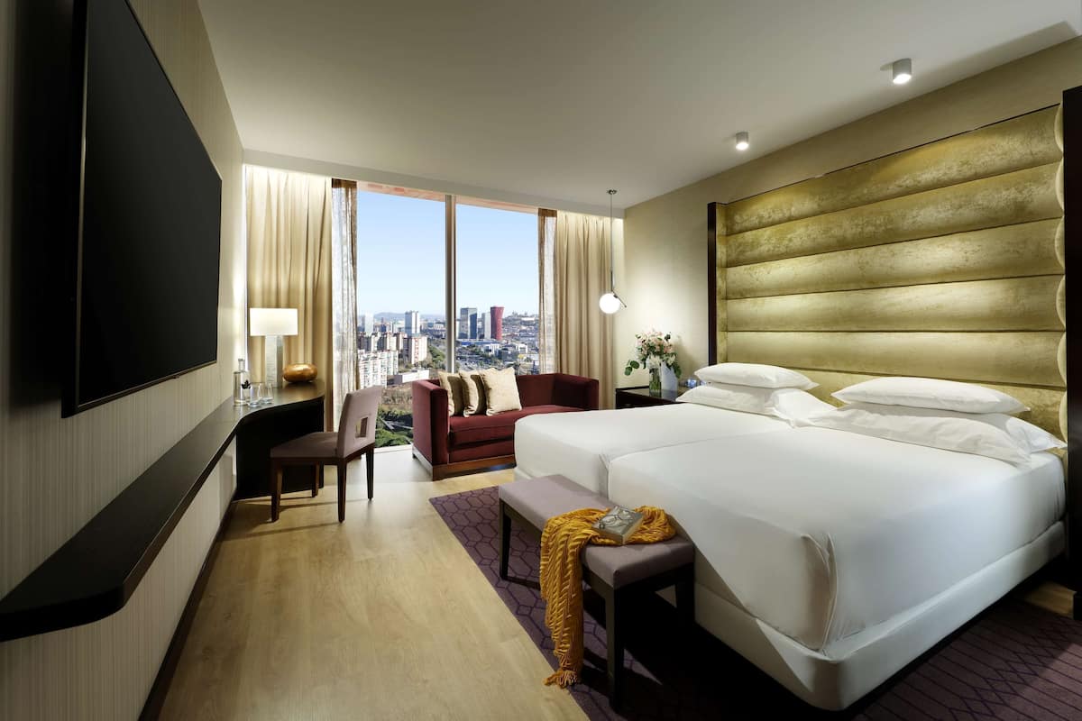 A hotel room with a large bed, a sofa, a TV, and a city view.