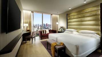 Quarto de hotel com uma cama grande, um sofá, uma televisão e vista para a cidade.