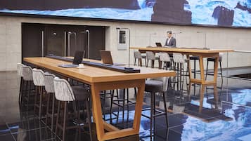 A modern conference room with a large screen displaying a scenic ocean view, wooden tables, and bar stools.