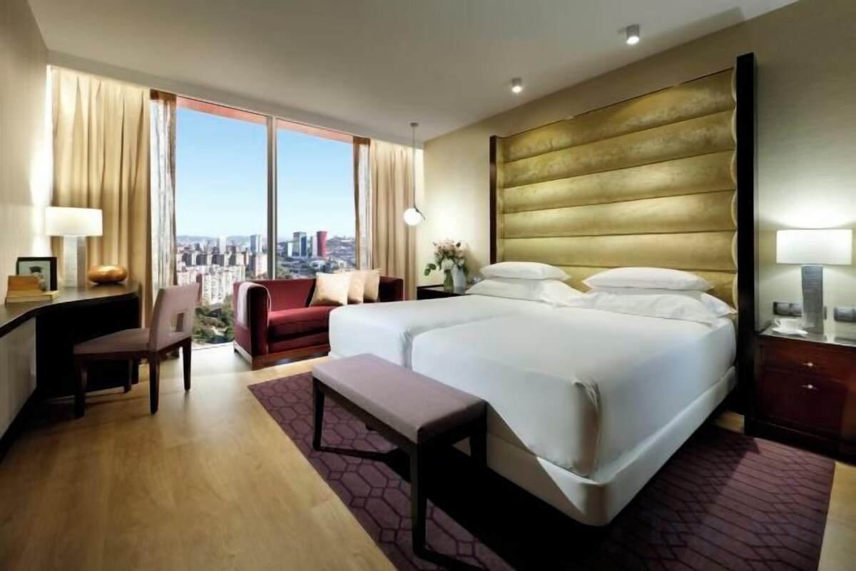 Ein Hotelzimmer mit einem großen Bett, einem Schreibtisch, einem Stuhl und Blick auf die Stadt.