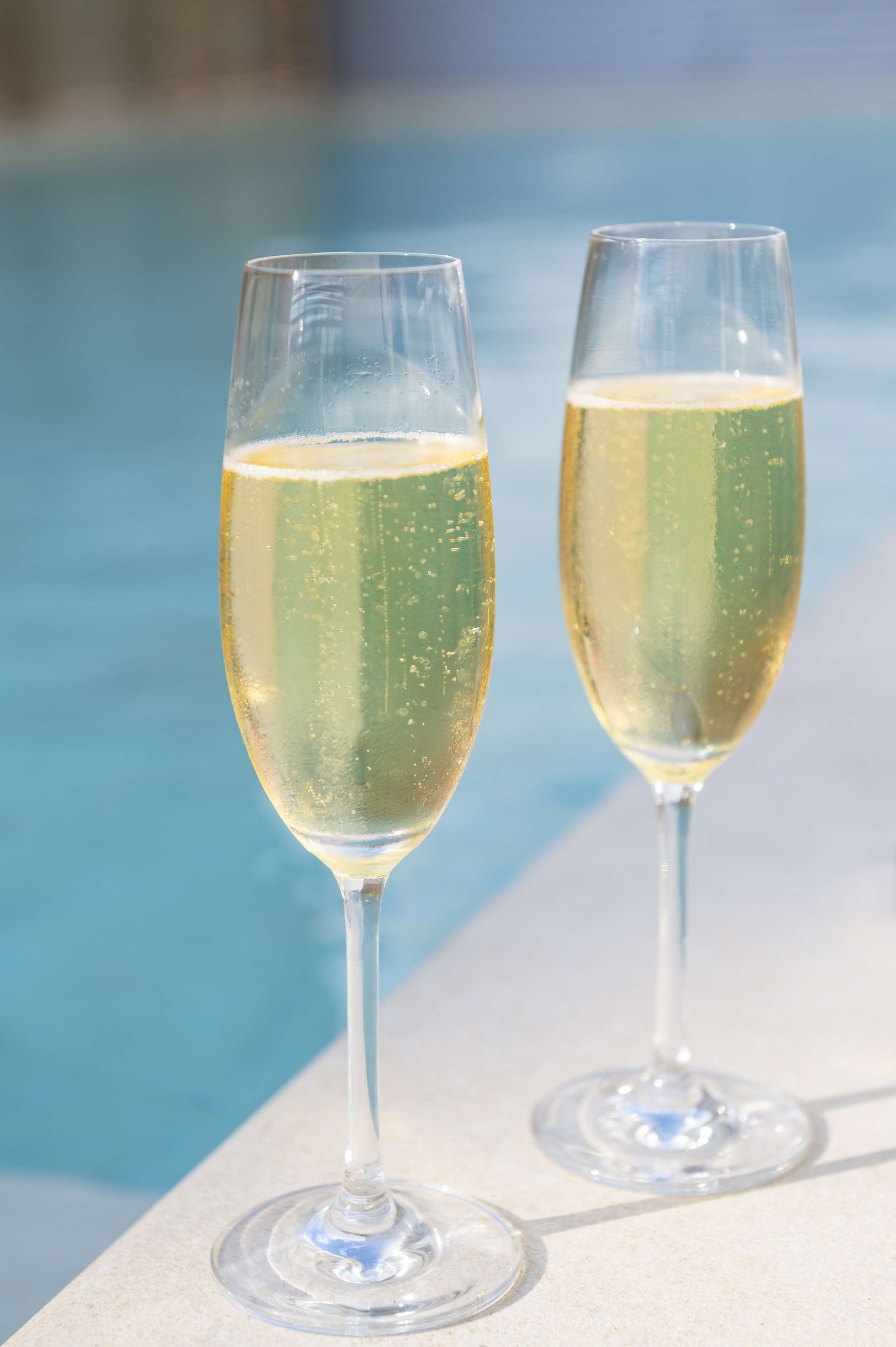 Two champagne glasses by a poolside.