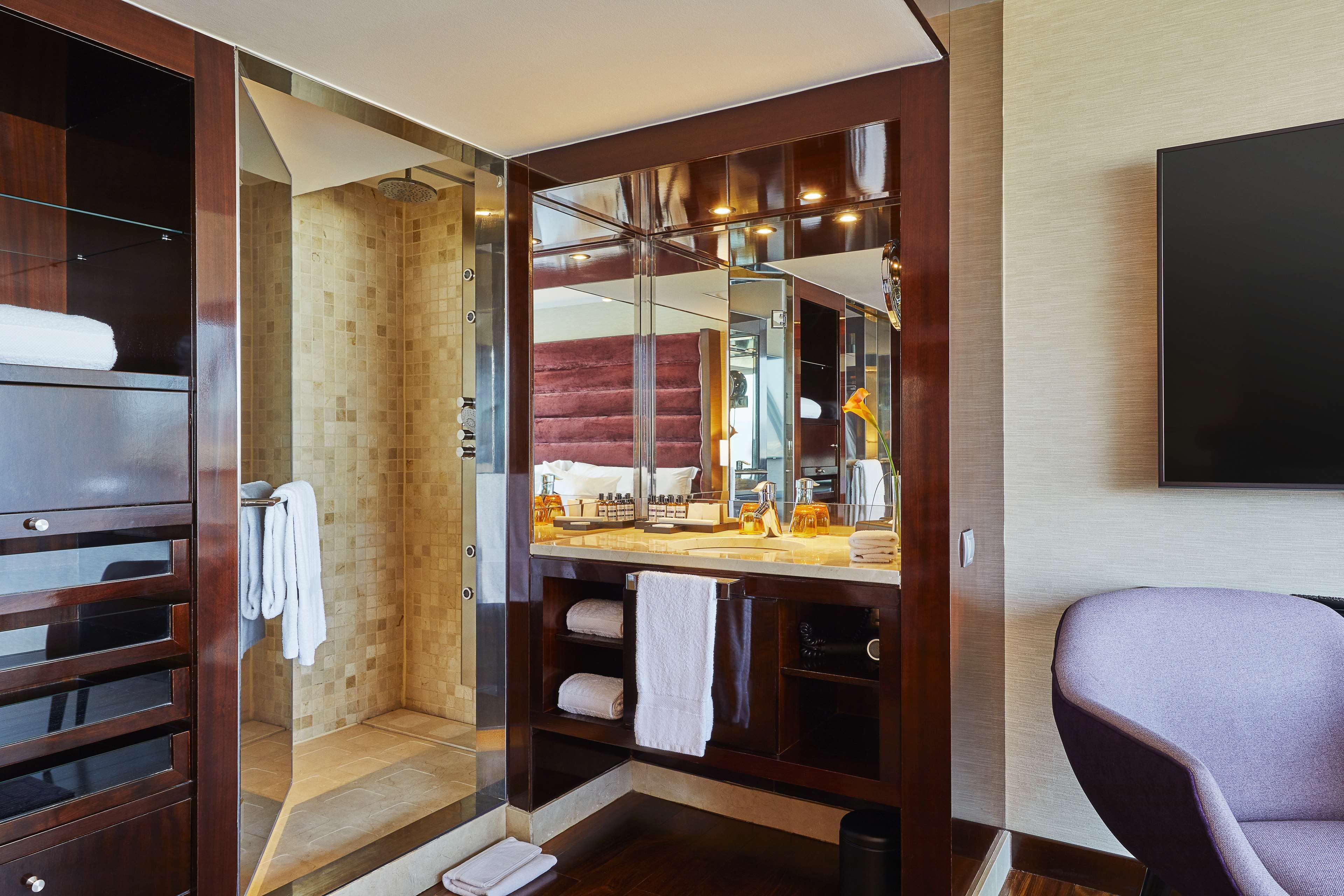 A modern bathroom with a walk-in shower, a vanity with a mirror, and a seating area.