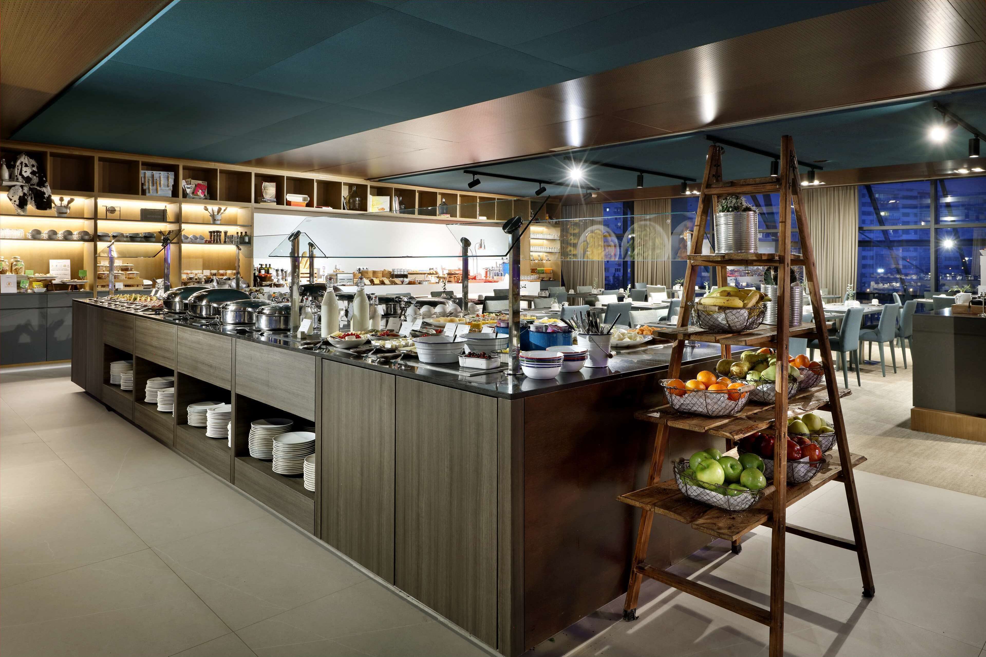 A modern kitchen area with a central island, shelves with kitchenware, and a fruit display.