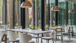 Un espace de restauration intérieur moderne, doté de tables et de chaises en verre, de grandes fenêtres et de luminaires suspendus.