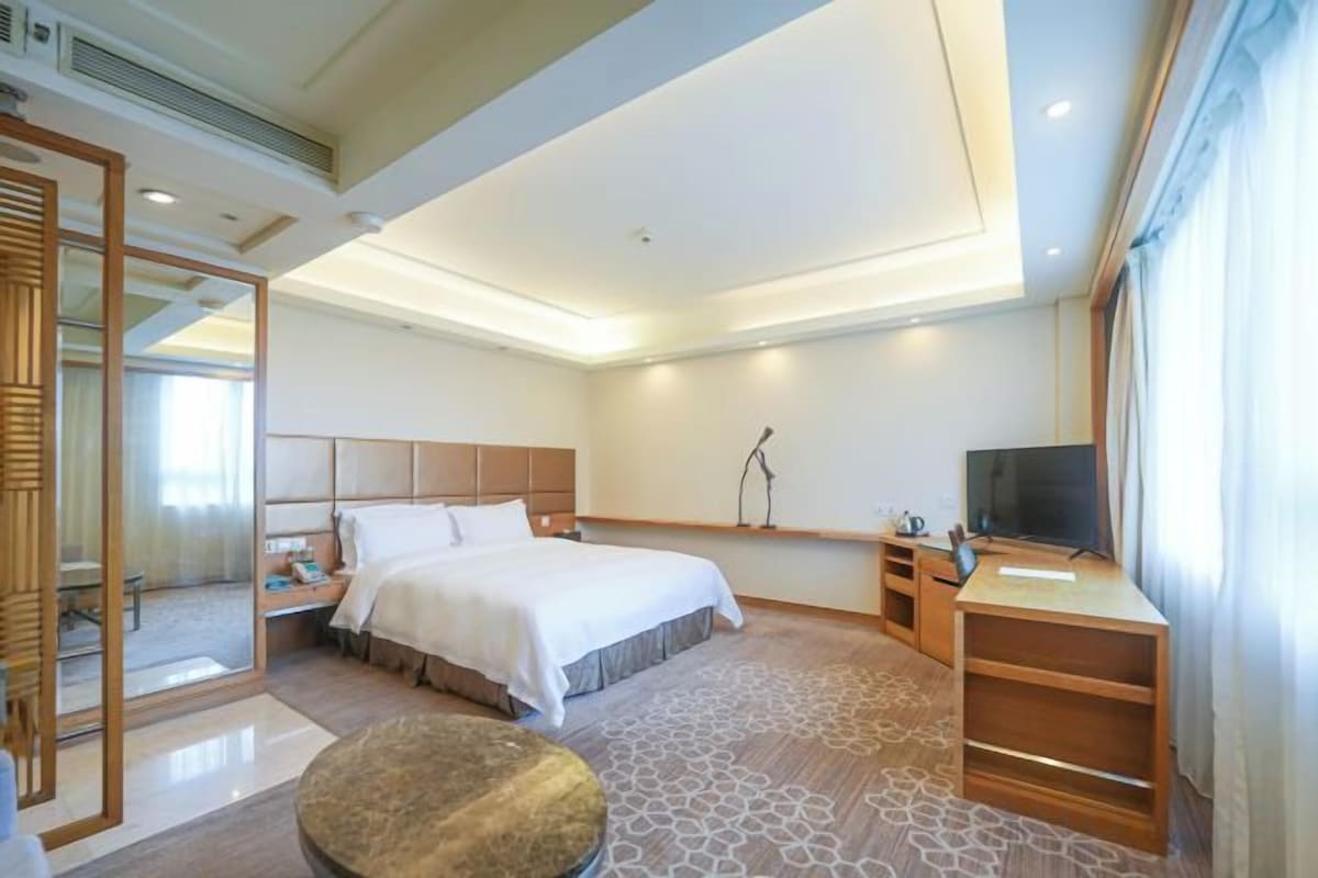 Habitación de hotel con cama, mesita de noche, televisor y zona de estar con una mesa redonda.