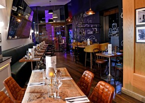 Un interior de restaurante con mesas de madera, asientos de cuero tipo banqueta y un mural en la pared.