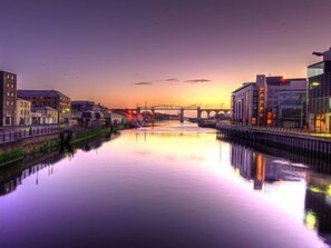 Un río con un puente, edificios a ambos lados y un atardecer.