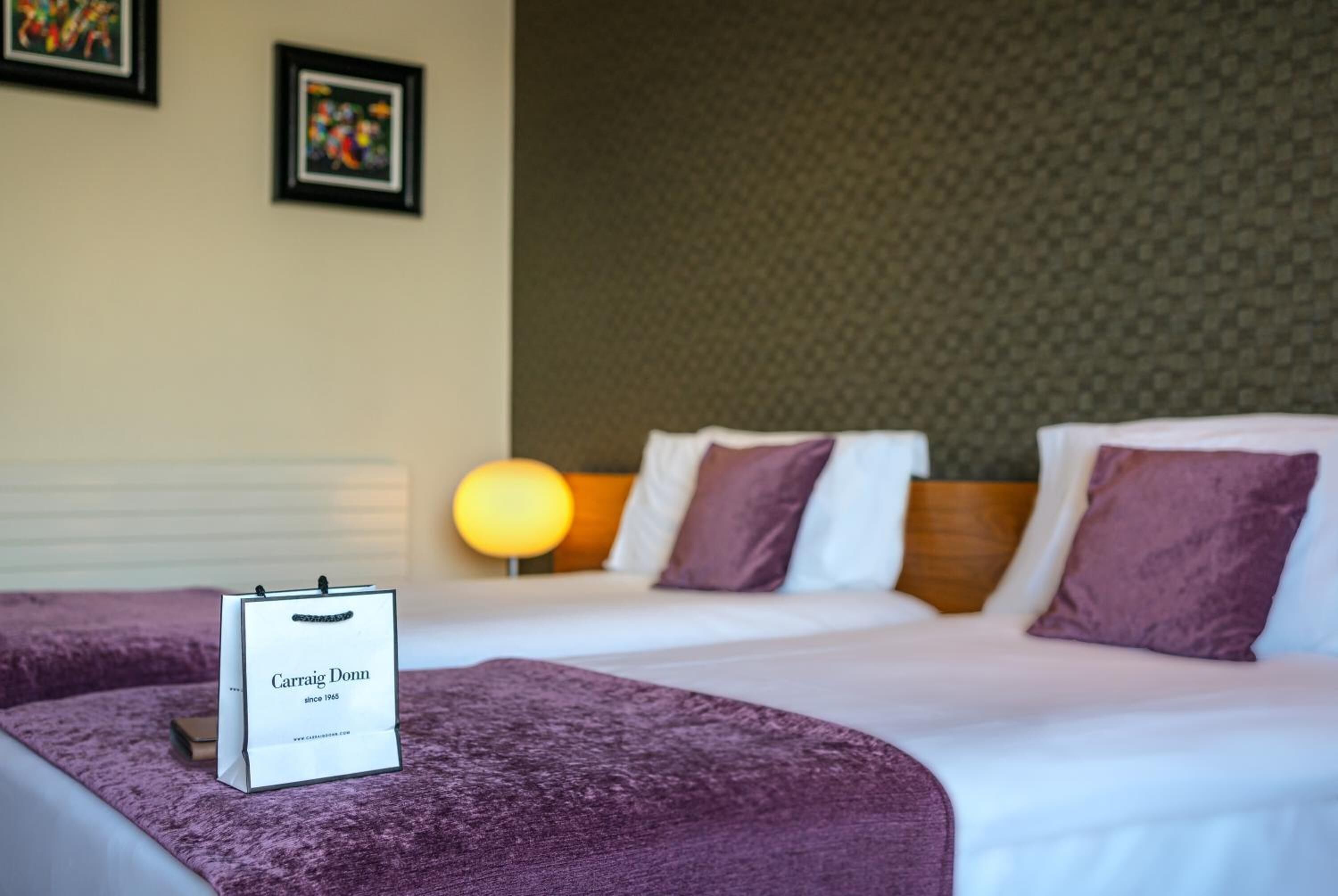 Habitación de hotel con dos camas, una colcha morada, un cartel enmarcado y una pared texturizada.