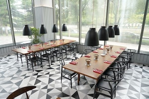 A dining area with a long table, multiple chairs, black pendant lights, and a geometric patterned floor.
