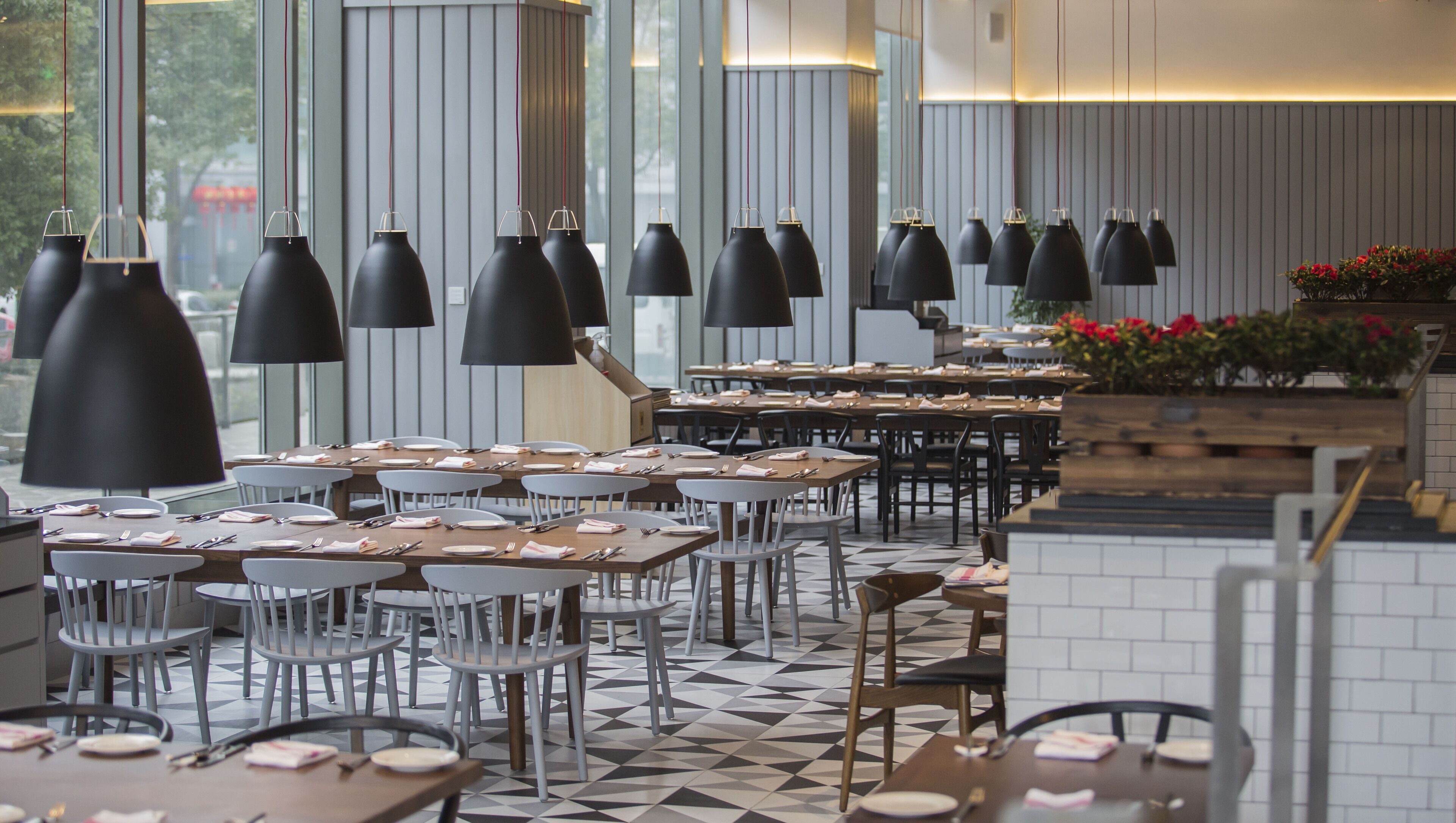 A restaurant with multiple tables and chairs, black pendant lights, and a tiled floor.