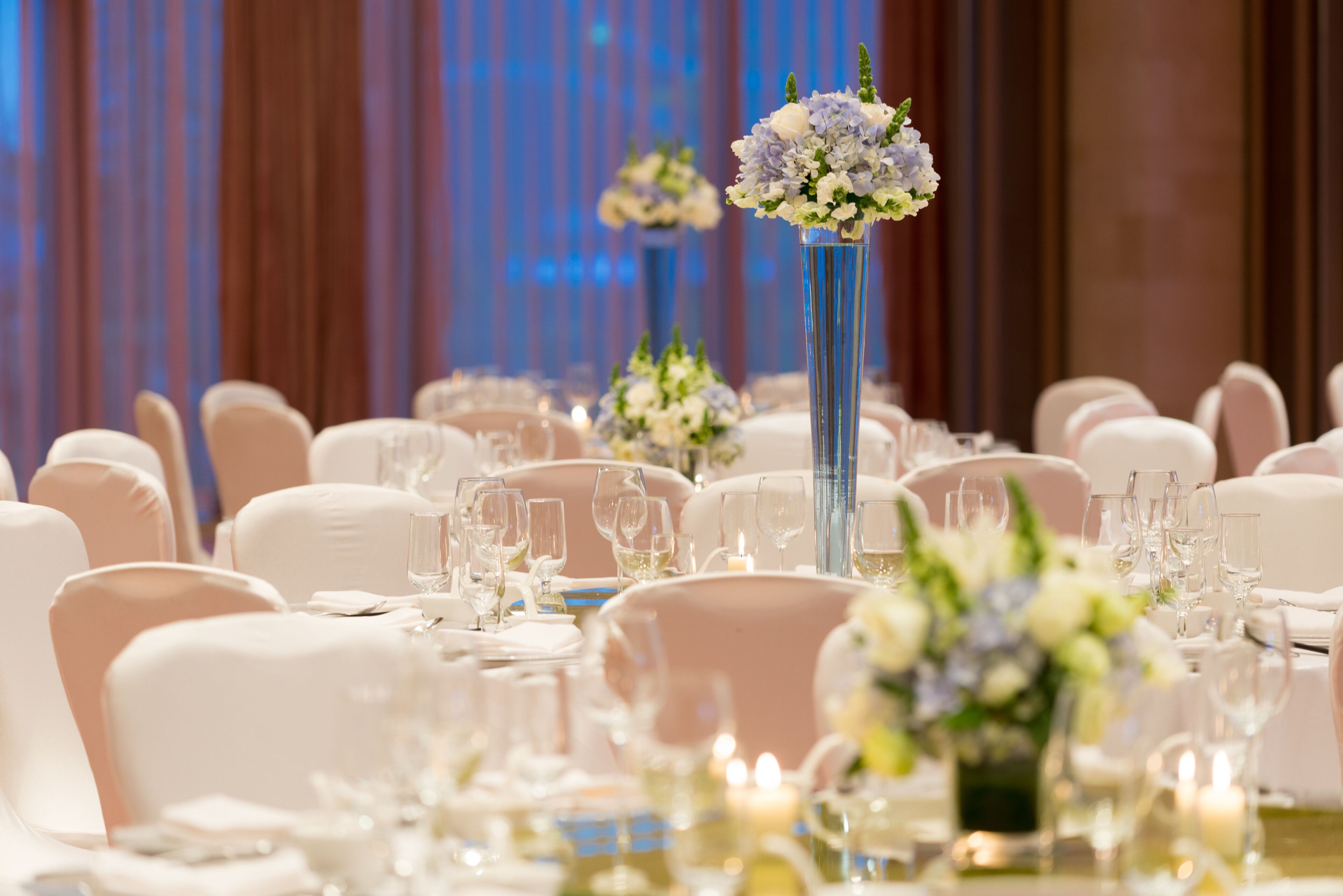 A banquet hall with round tables set for a formal event, featuring white tablecloths, glassware, and floral centerpieces.