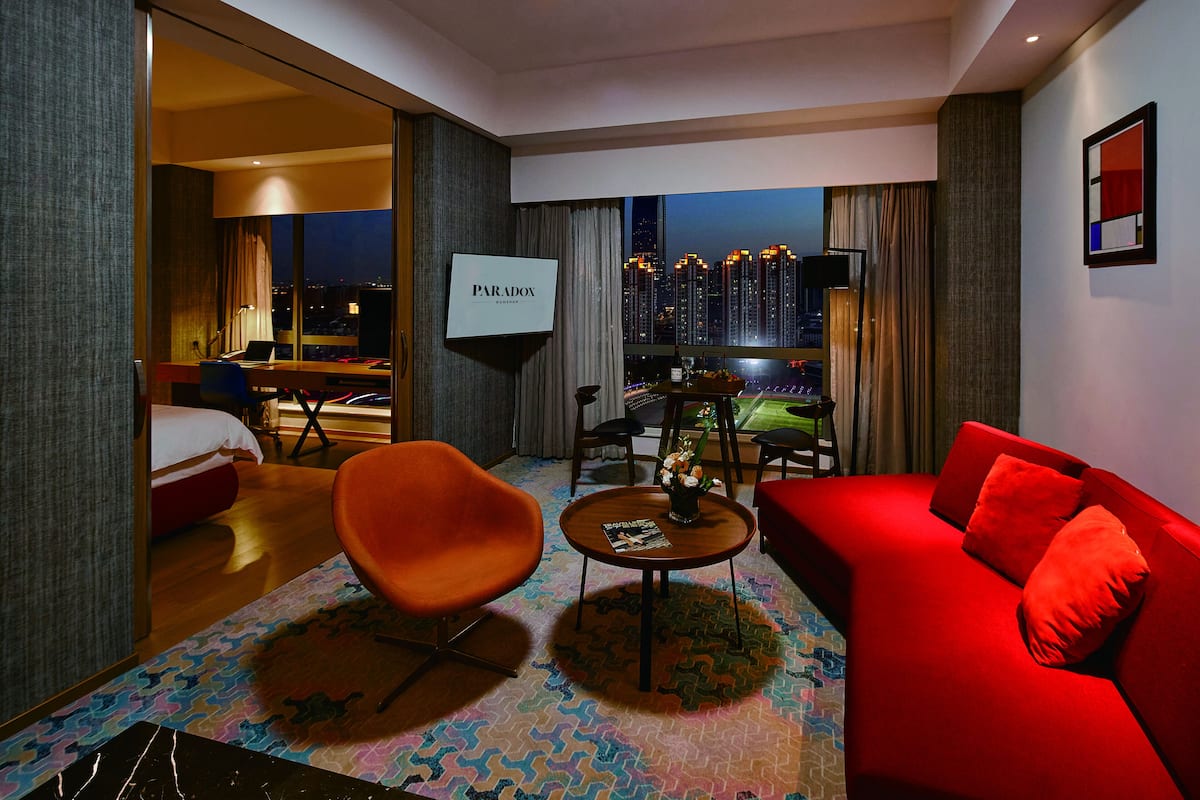 A modern hotel room with a red sofa, orange chair, and a TV screen displaying "PARADOX".
