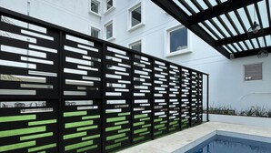 A modern pool area with a clear view of the pool, a black and white fence, and a building in the background. - Fato Hotel (Querétaro)