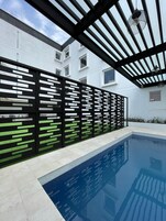Un área de piscina moderna con vista despejada, una valla blanco y negro, y un edificio al fondo.