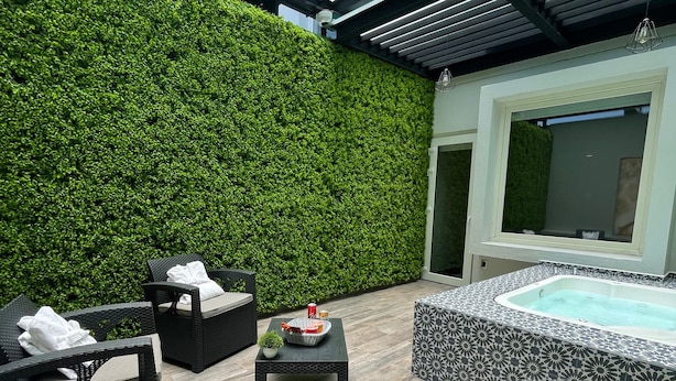 A modern outdoor area with a green wall, a hot tub, and wicker furniture. - Fato Hotel (Querétaro)