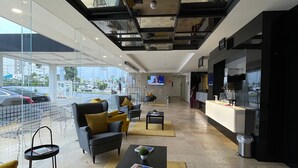A modern interior with a glass wall, a reception desk, a sofa, and a coffee table. - Fato Hotel (Querétaro)