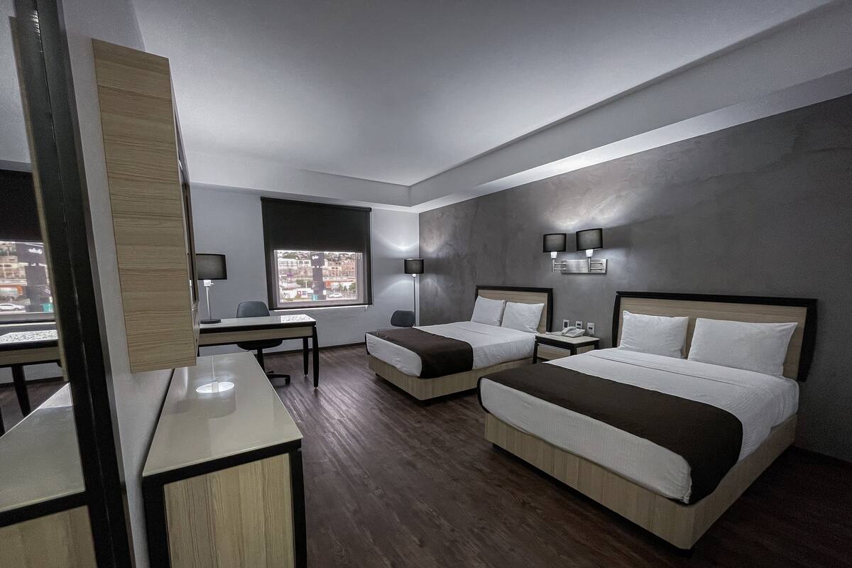Moderni hotellihuone, jossa on kaksi sänkyä, työpöytä ja näkymä kaupunkiin.