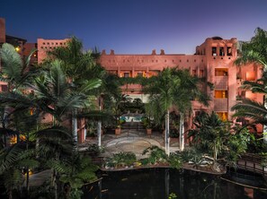 A resort with a pool, palm trees, and a large building with multiple balconies.