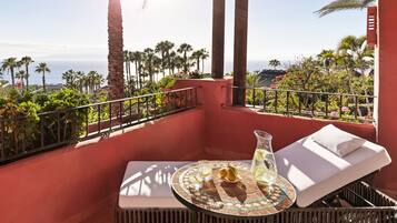 Un balcon avec une table, un fauteuil et une vue sur l’océan et les palmiers.