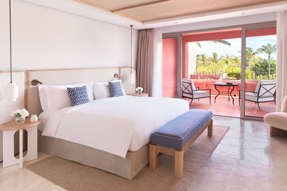 Habitación de hotel moderna con una cama grande, una mesita de noche, un banco y vistas al exterior.