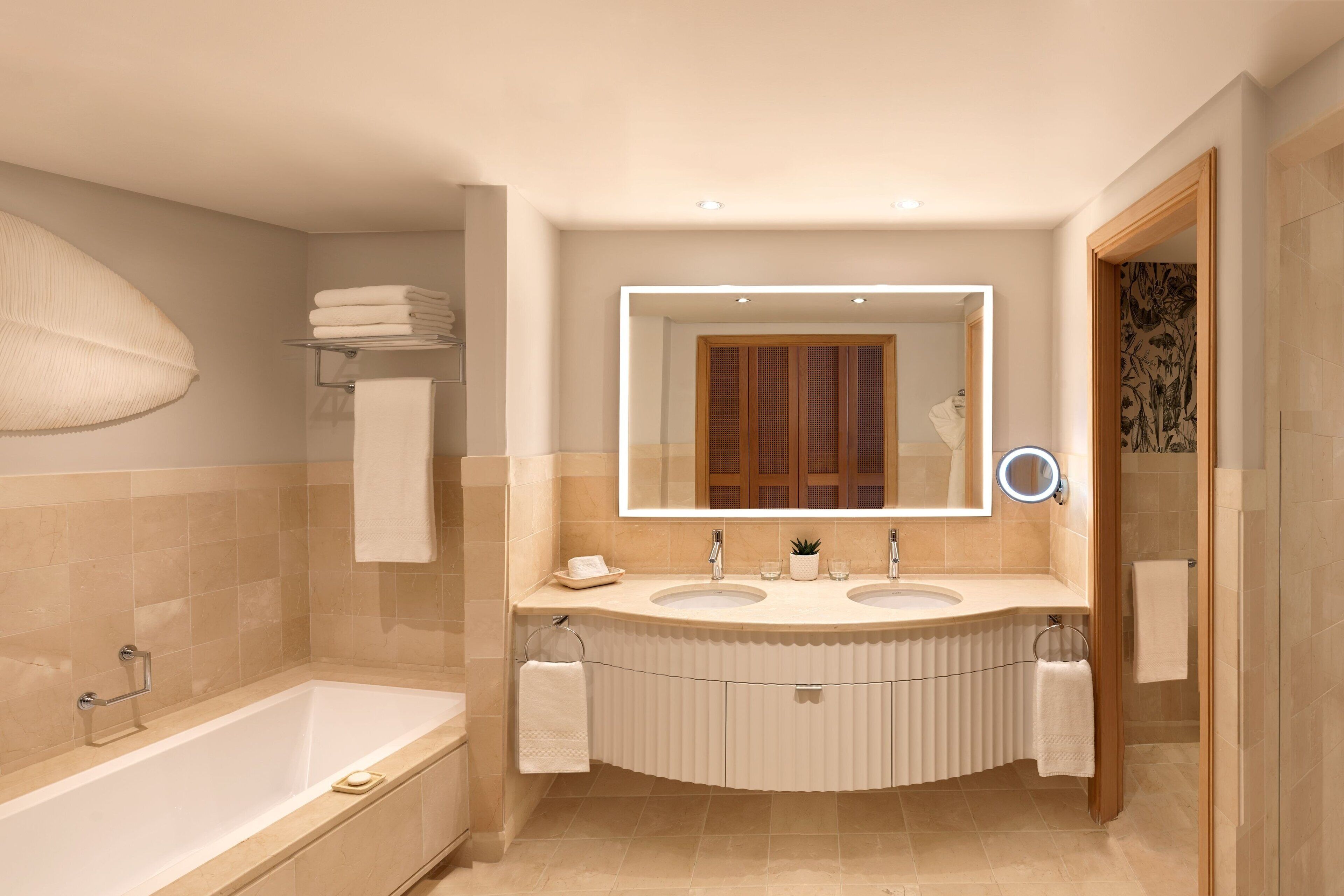 Un baño moderno con una bañera, dos lavabos, un tocador y un espejo grande.