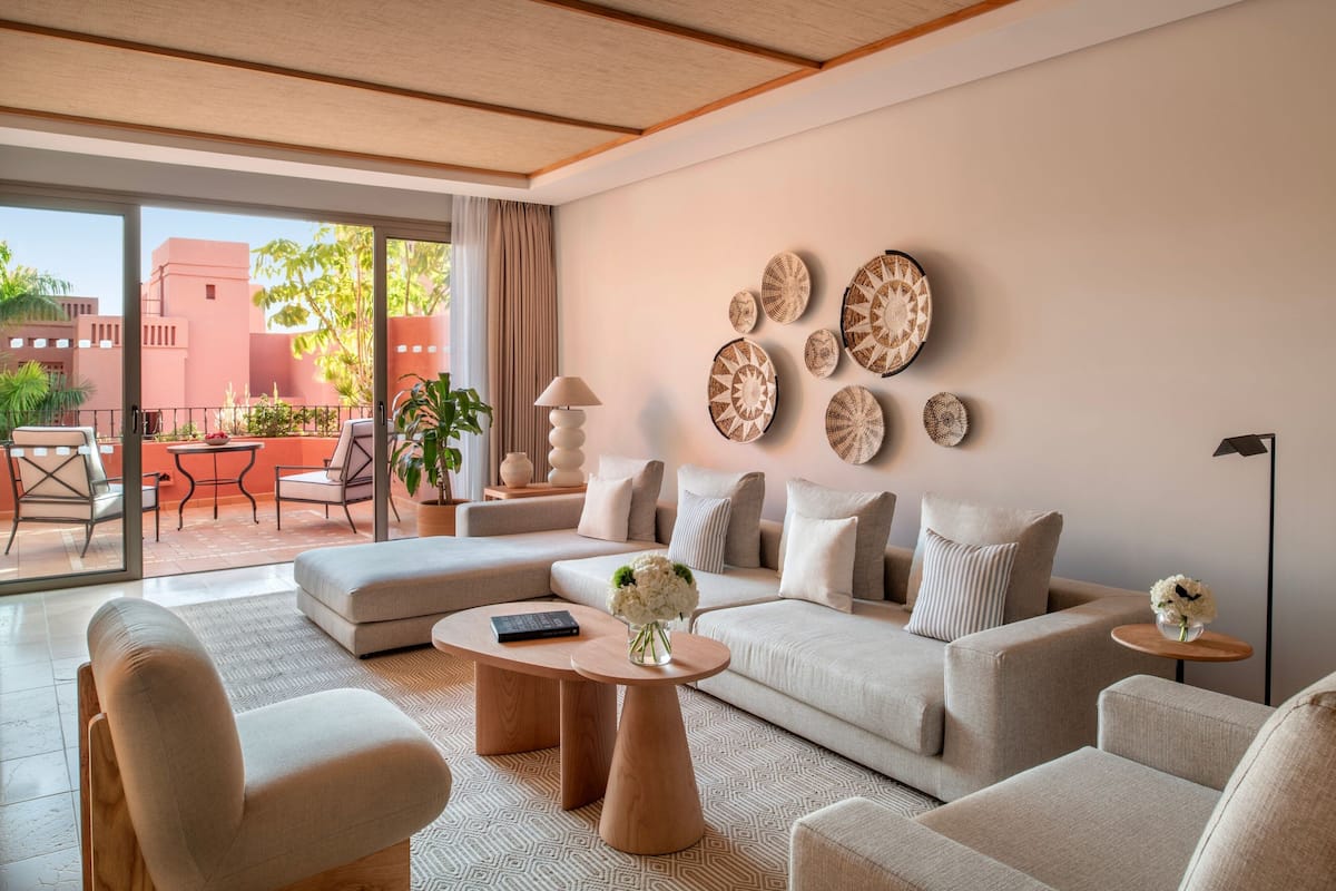 Una sala moderna con un sofá, sillones y una mesita de centro. Se observan elementos decorativos en la pared y vistas al exterior.
