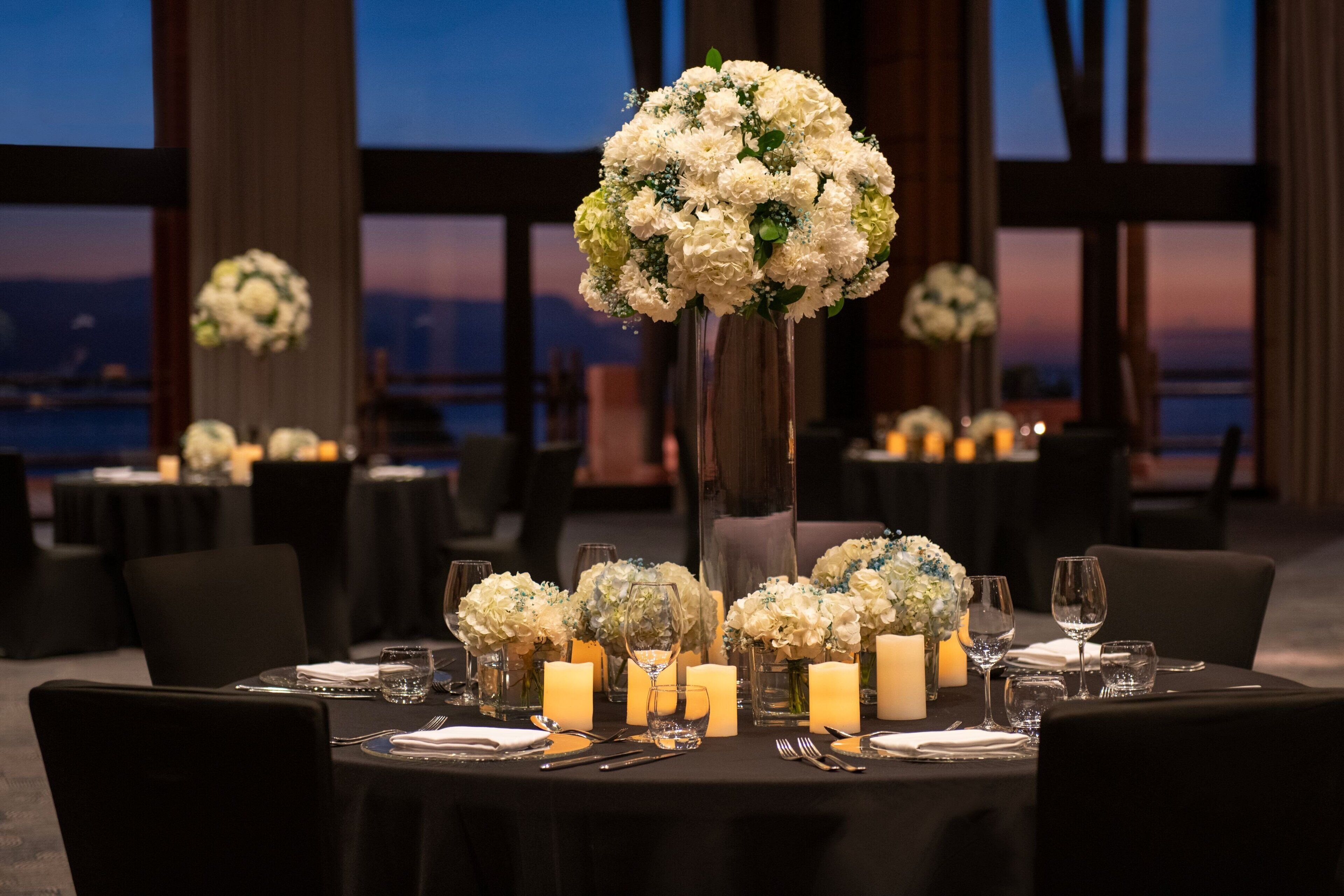 Un comedor con mesas dispuestas para un evento formal, con centros de mesa florales y velas.