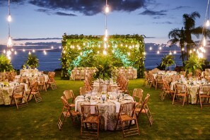 An outdoor wedding reception with round tables, wicker chairs, and string lights. - The Ritz-Carlton Tenerife, Abama (Guia de Isora)