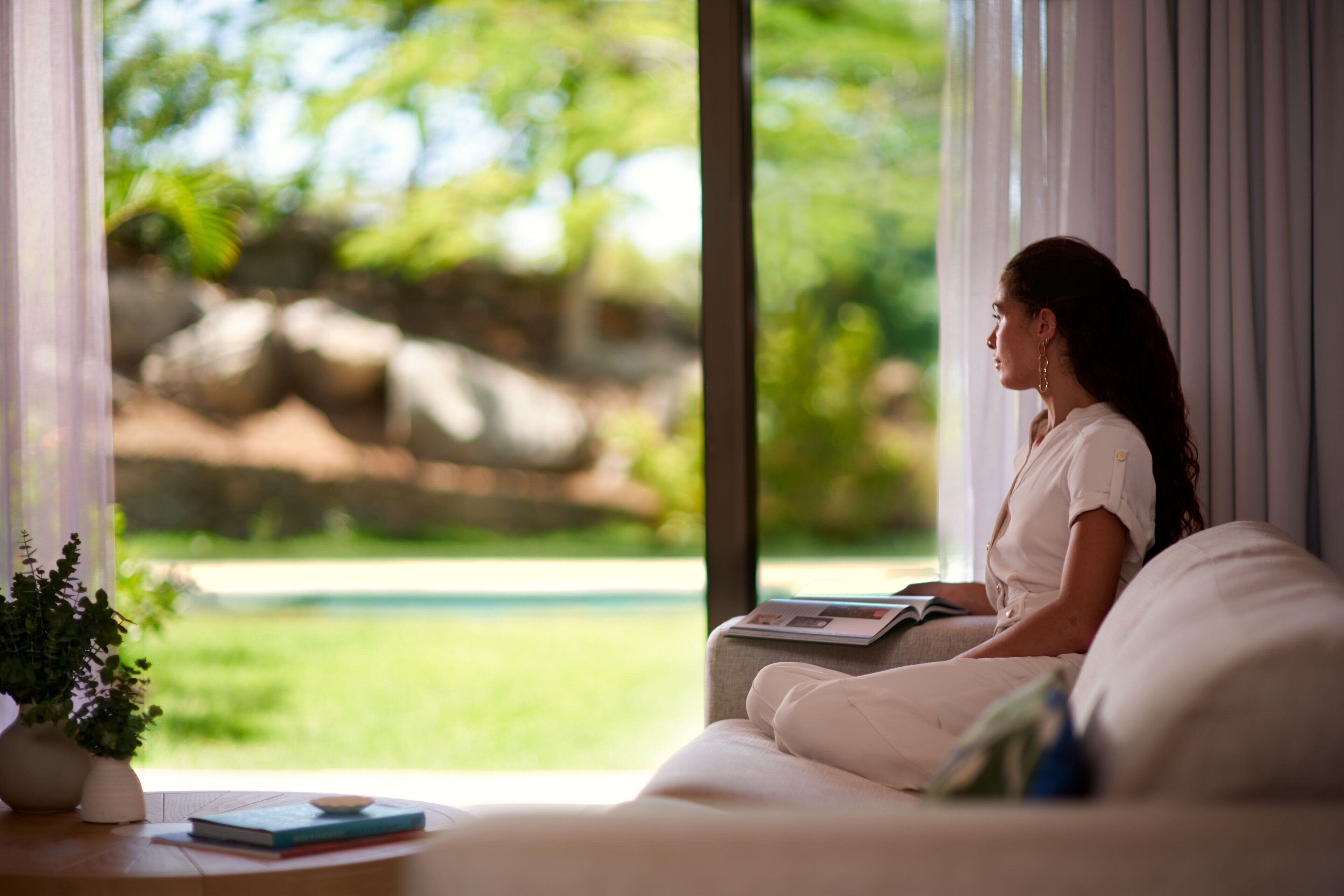A person sitting on a sofa by a window with a view of greenery and rocks.