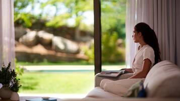 A person sitting on a sofa by a window with a view of greenery and rocks.