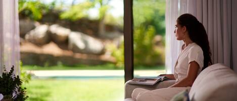 A person sitting on a sofa by a window with a view of greenery and rocks.
