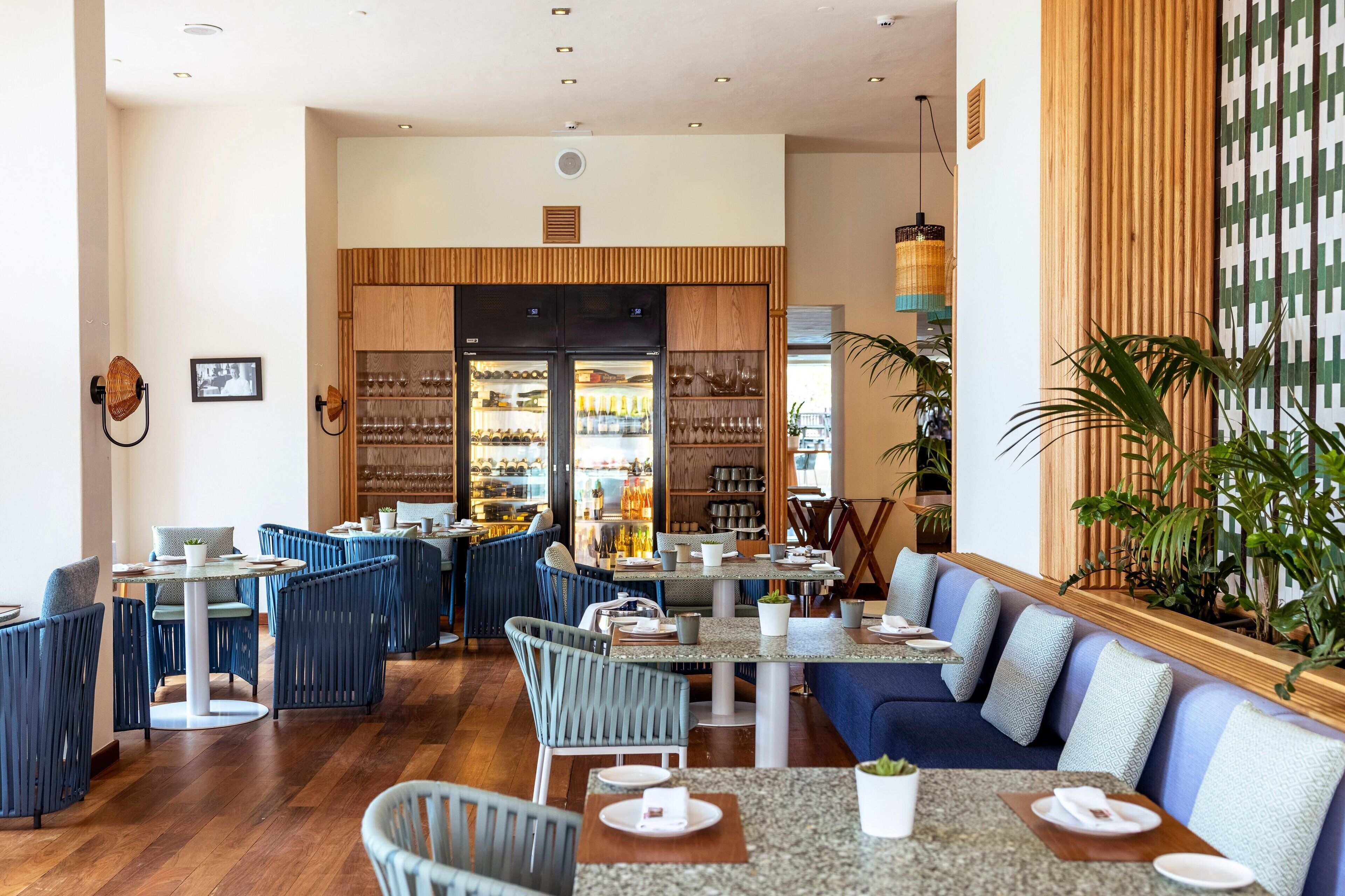 A modern restaurant interior with wooden accents, blue seating, and a variety of table settings.