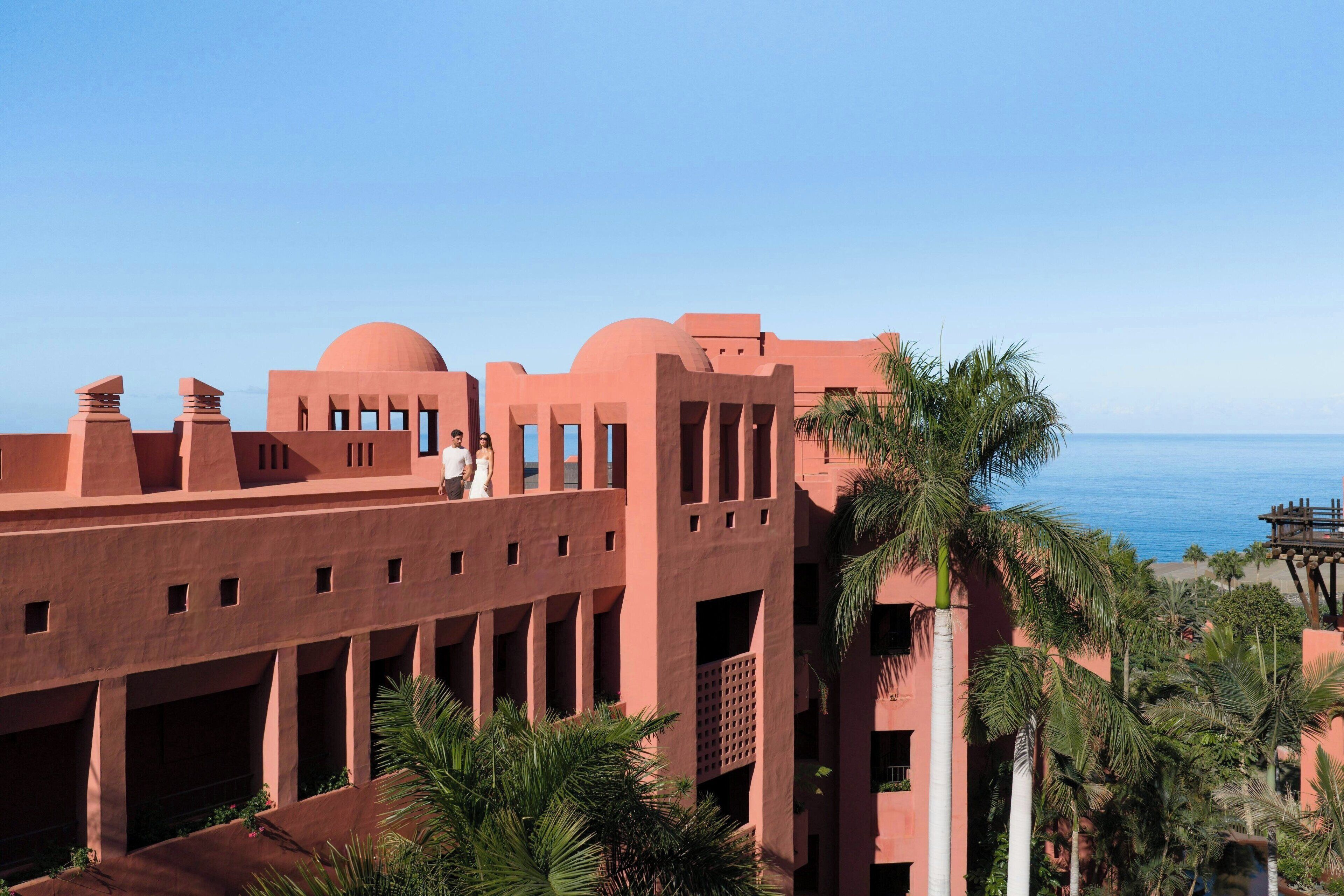 Un edificio con fachada de terracota, varios balcones y palmeras.