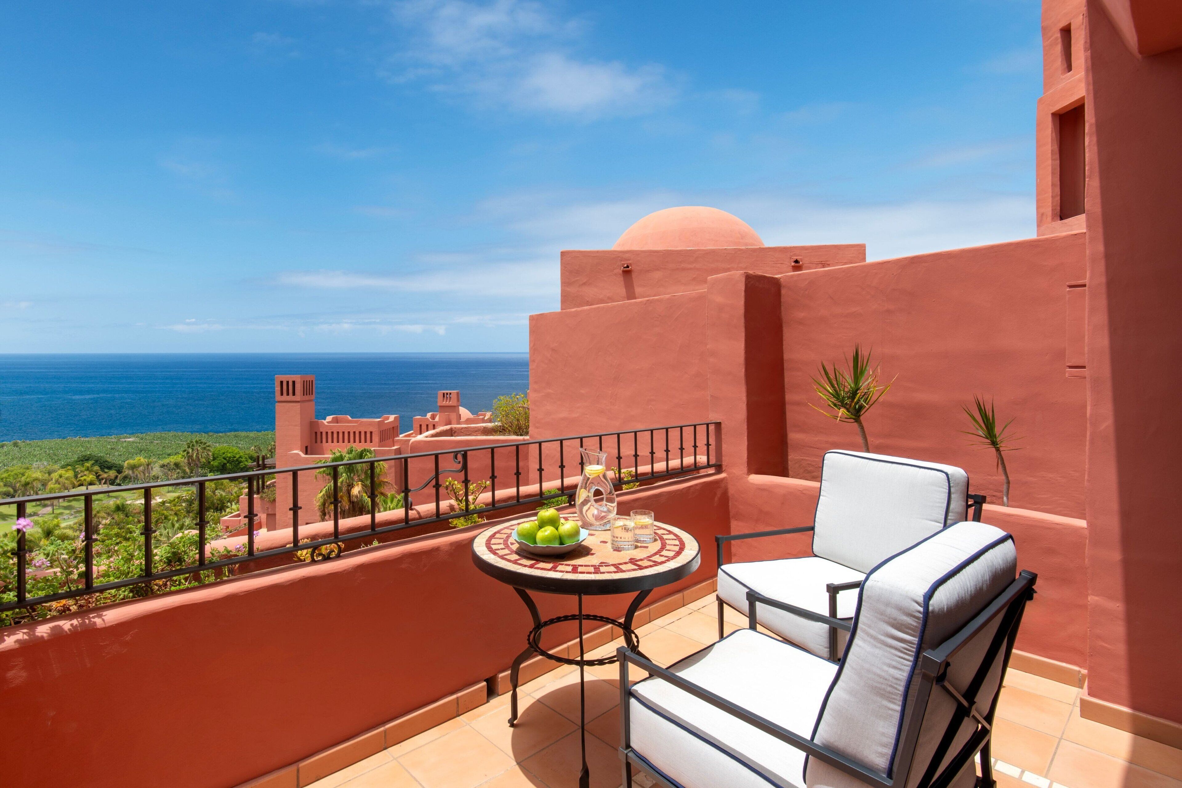 A balcony with a table, chairs, and a view of the ocean.