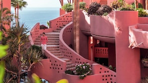 A pink building with a spiral staircase and palm trees.